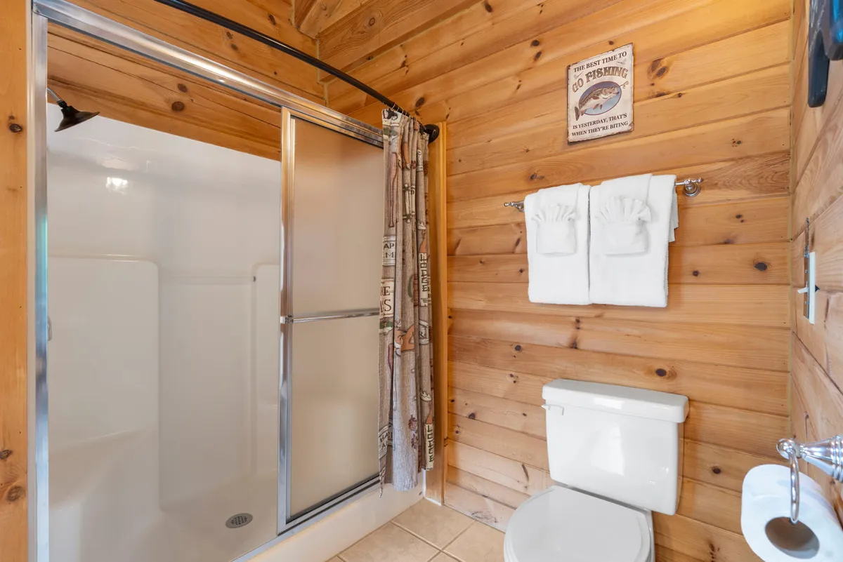 A walk-in shower set against wooden wall panels, with plush towels and fishing-themed decor adding character. The space feels tranquil and inviting, ideal for refreshing starts or unwinding after a day’s adventures.