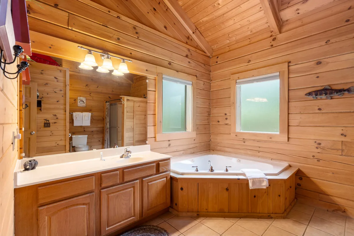 An inviting interior scene featuring a jacuzzi tub with natural light streaming through the windows, set against wooden walls. The space exudes tranquility and hints at post-adventure relaxation.