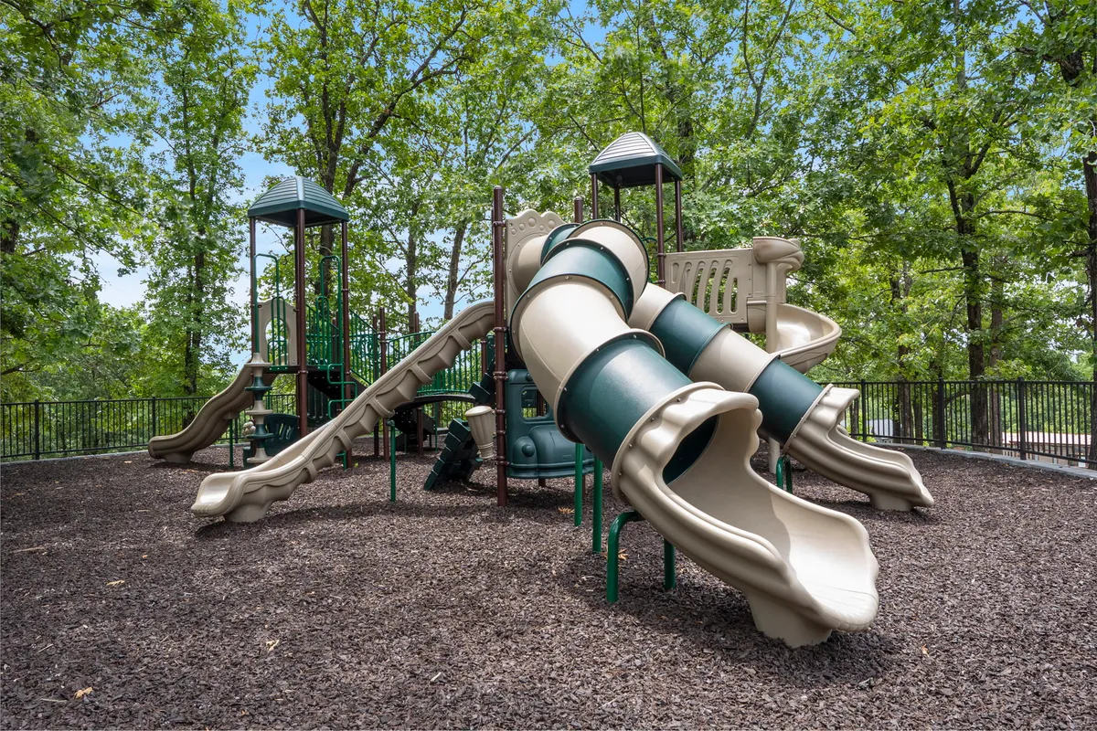 A colorful playground featuring slides and climbing structures cradled by leafy trees, with children playing and families gathering nearby. The mood is joyful and energetic, capturing laughter-filled afternoons.