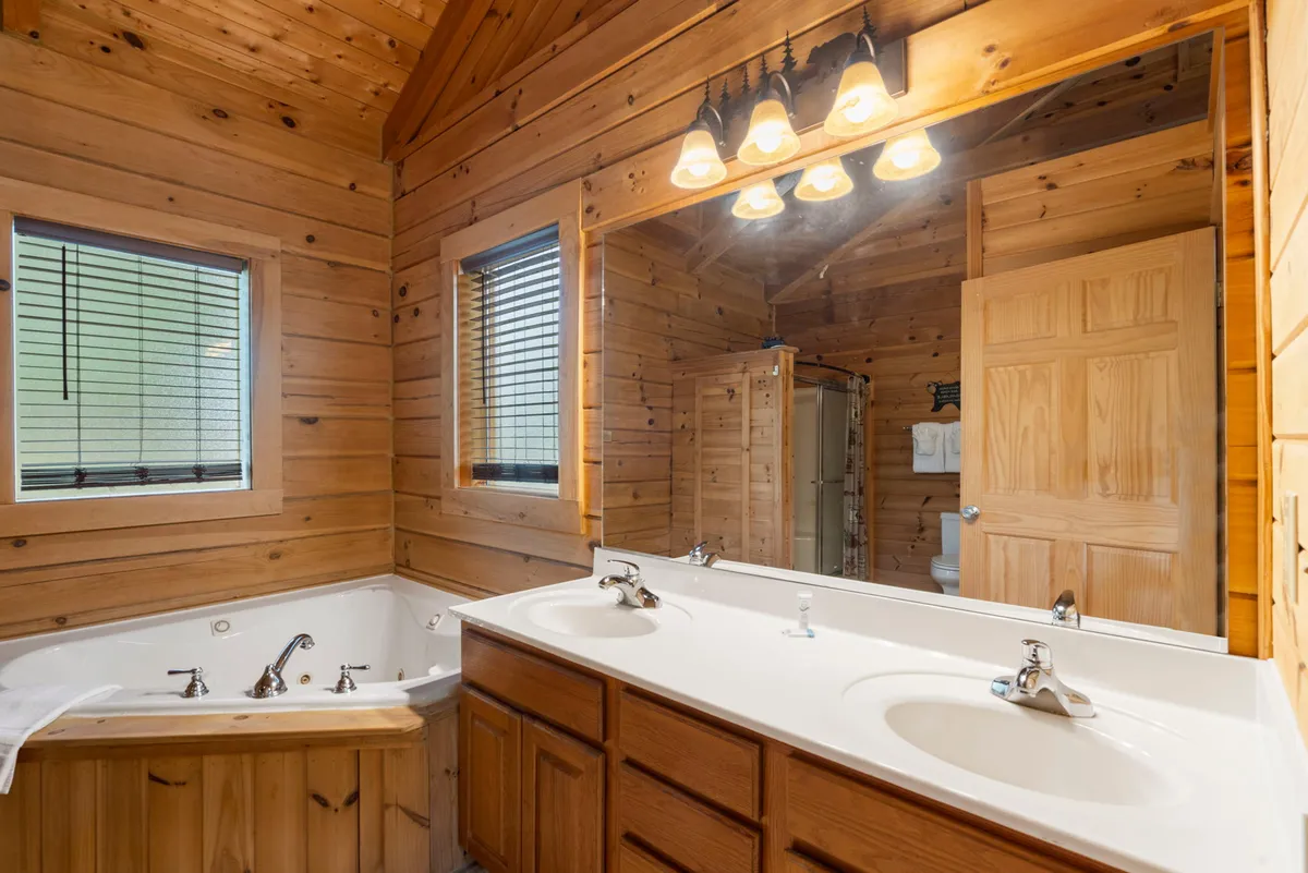 A luxurious master bathroom with a jetted jacuzzi tub, double sink vanity, expansive mirror, and warm wooden paneling. Natural light streams in, highlighting the tranquil, spa-like ambiance perfect for relaxation and self-care routines.