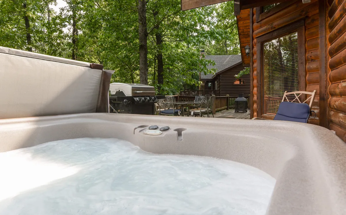 This image showcases a wooden back deck with a private hot tub surrounded by lush greenery. The inviting scene hints at relaxing evenings spent soaking in warm bubbles, with the tranquility of nature just beyond the deck railing.