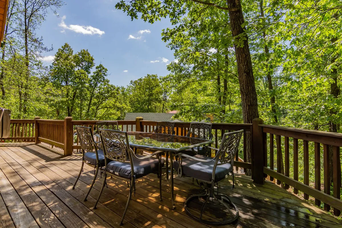 An outdoor deck is furnished with an inviting dining set, bordered by lush trees and a simple railing. The space is designed for relaxation, outdoor meals, and unwinding after a day of activities, with a peaceful view of nature all around.